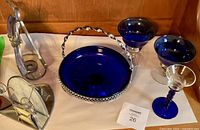 Photo showing cobalt blue glass candy dish with silver holder and handle along with cobalt blue and clear glass stemware and a metal kitchen tool.
