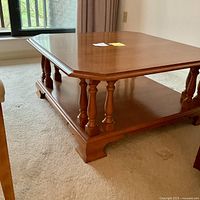 Side view of the wood coffee table showing the turned legs, lower shelf, and polished medium brown finish.