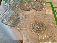 Photo showing 3 small crystal bowls with starburst pattern, 2 medium cut glass bowls with diamond sides, and a large clear glass platter with etched floral design and scalloped edges.