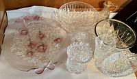 Eight pieces of vintage pressed and cut glassware including punch bowls, candy dish, decanter, oil dispenser, vase, and floral accent bowls.