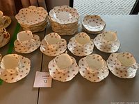 8 cups arranged in two rows in front of stacks of saucers and side plates showing pattern and gilded edges