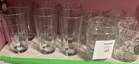 Tall clear drinking glasses and clear textured beer mugs grouped together on a shelf.