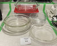 Full view of eight pieces of clear glass bakeware placed on a counter, including a square dish with lid, one pie plate, and four bowls.