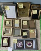 Fifteen assorted picture frames arranged on the floor with size labels attached to each frame.