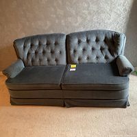 Front view of blue 2-seater loveseat sofa with button tufting on backrest and armrests, placed on a carpeted floor against a wallpapered wall.