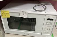 Front and side view of white Panasonic Genius 1100W microwave on countertop, showing the keypad, display, and glass window door.