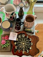 Full view of lot including two pitchers with floral and cracked patterns, blue round vase, small dark vases, wooden wall clock with floral face, boat in bottle, and pink rose bouquet corners.