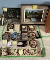 Photo showing entire lot of framed pictures, plate, needlepoint embroidery, plaques, and wooden stands with sticky notes showing measurements.