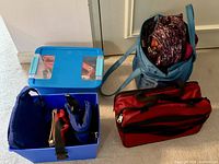 Full view of the blue plastic bin with lid containing folded bags, blue fabric tote bag filled with gift bags, and red soft-sided bag.