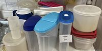 Various translucent plastic food storage containers with white, blue, and red lids, including several cereal containers and stackable round containers.