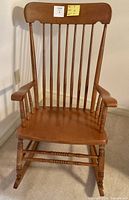 Front view of the solid wood rocking chair showing the wide curved backrest with vertical spindles, turned legs and arm supports, and contoured seat.