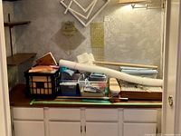 Shows shelves and countertop with various sewing and quilting supplies including frames, pattern papers, storage boxes with tools, and books.