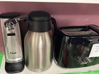 Front view of the three appliances: can opener, insulated coffee pot, and toaster from left to right placed against a pink wall