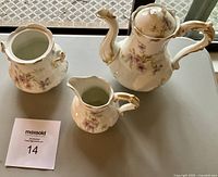 Photo of the tea set items showing teapot with lid, sugar dish, and creamer on grey surface near window