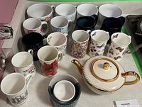Photo showing teapot with gold details and 16 assorted mugs with varied prints.