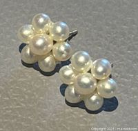 Pair of flower-shaped cluster stud earrings with white seed pearls on a grey surface, seen from the front showing the pearl clusters.