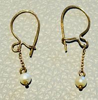 Close-up view of earrings showing yellow gold hooks, chaining and single dangle seed pearls.