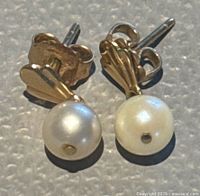 Close-up of 14K yellow gold pearl stud earrings lying on textured surface showing front view of pearls and gold backs.