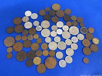 Over 70 mixed collectible coins spread on a blue surface, showing a variety of metals and sizes.