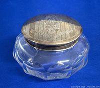 Front angled view of antique silver topped glass powder pot showing engraved floral design on lid.