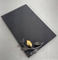 Top angle of black granite cheese board with bronze and gold lemon decorative accent at one corner.