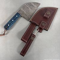 Damascus chef cutting tool with blue-streaked handle and original brown leather sheath shown apart on a surface.