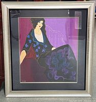 Full view of the framed print showing the stylized woman seated with colorful patterns and the silver frame.
