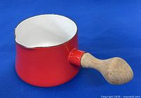 Front side view of the small red enamel saucepan showing the white interior and wooden handle.
