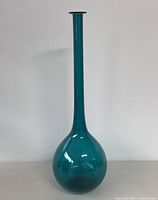Full view of the teal blue Empoli genie glass bottle vase showing its tall narrow neck and round base against a white wall