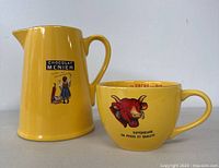 Yellow ceramic pitcher and mug side by side showing graphic details and shape.