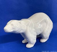 Porcelain polar bear figurine on blue background, showing right side profile and stance.