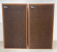 Front view of both speakers with fabric grills on, showing wooden frames and Ohm logos at top left corner.