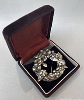 Brooch displayed inside a vintage brown velvet jewelry box with red satin lining on the inside of the lid.