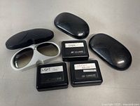 White frame sunglasses with installed gradient lenses, three smooth black cases and three lens storage boxes labeled Dark, Light Pol, Standard Brown