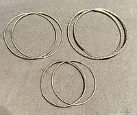 Set of three pairs of silver hoop earrings arranged on grey fabric, showing different diameters and surface textures.
