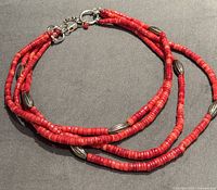 Full view of four strand red coral necklace with silver spacers and clasp laid flat on a dark surface.