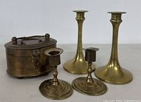 Front view of the full lot showing two tall and two short brass candle holders along with an oval brass jali box.