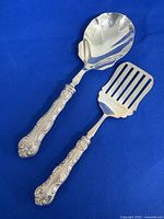 Two sterling silver servers with ornate handles on blue background.