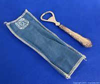 Bottle opener with ornate sterling silver handle and fabric pouch on blue background.