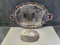 Front view of large ornate Wilcox International Silver Co. silver plated on copper tray with handles, showing embossed floral and scroll pattern and scalloped edges.