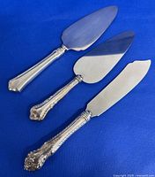 Three serving flatware pieces with sterling silver handles arranged on a blue surface showing overall shape and design