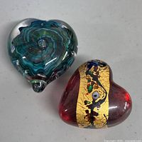 Two heart shaped art glass paperweights, one red with gold and enamel colors, the other multicolored with blue/green swirls