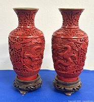 Pair of red cinnabar lacquer vases with detailed dragon and floral relief carvings on body, photographed on blue cloth.