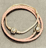 Two Pandora bracelets, one silver snake chain and one pink braided leather, both coiled together showing branded clasps