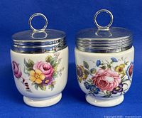 Pair of vintage Royal Worcester egg coddlers side by side showing floral designs and metal lids with ring handles