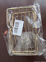 Photo of one gold tone metal soap box rack wrapped in clear plastic packaging with barcode sticker visible.