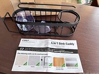 Photo of assembled 4 in 1 Sink Caddy with two suction cups and instruction pamphlet on a wooden surface.