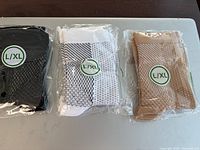 Three pairs of ankle compression socks - black, white with black dots, and beige with darker dots, sealed in clear plastic packaging, all size L/XL.