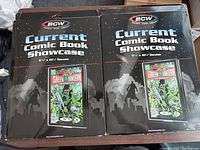 Two BCW Current Comic Book Showcase cases in original packaging, black with space to display a front comic book.