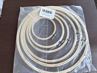 Photo showing sealed pack of six natural wood embroidery hoops in different sizes arranged in ascending diameter, with metal screw adjustable fasteners.